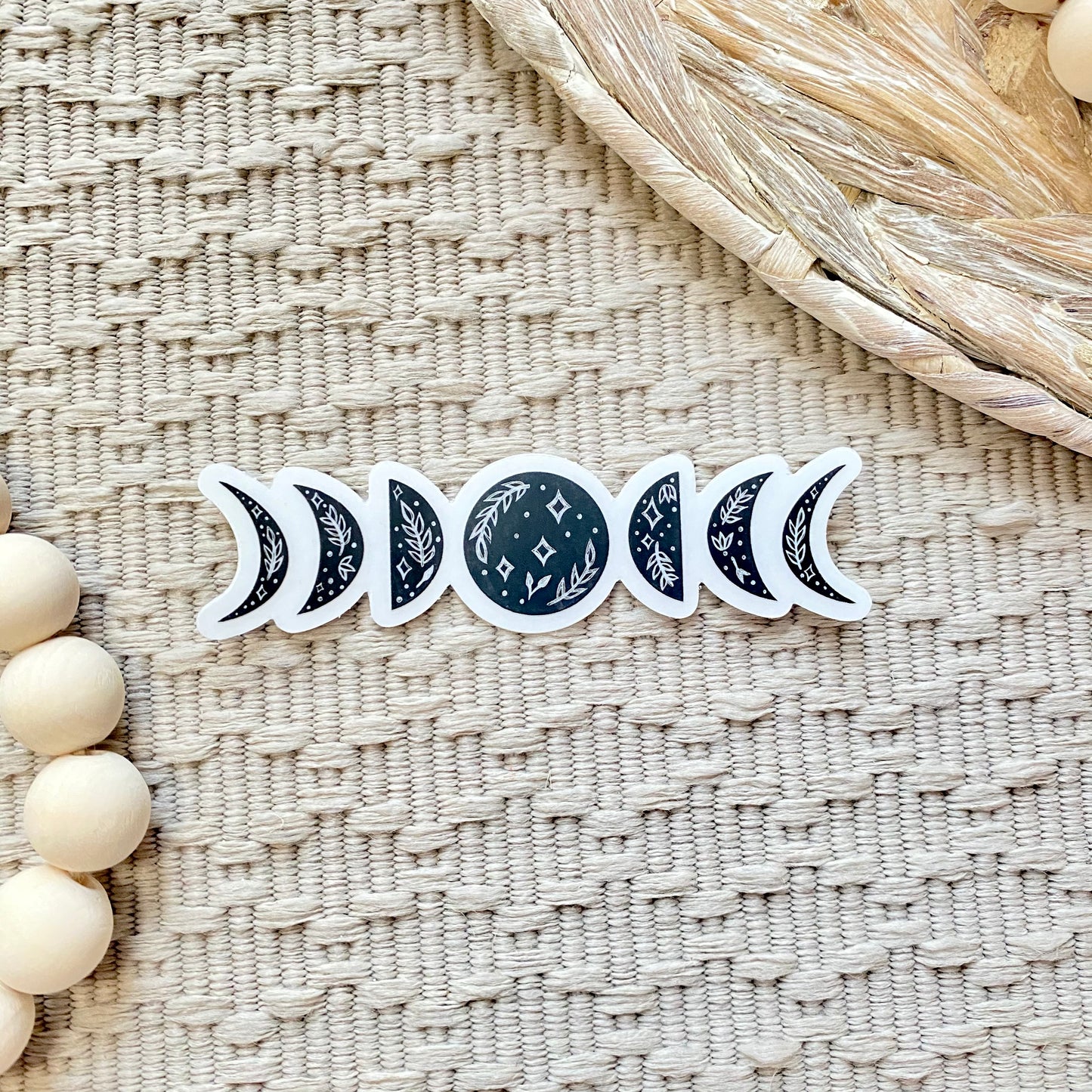 Set of black floral moon phase stickers on a textured woven surface with wooden beads.
