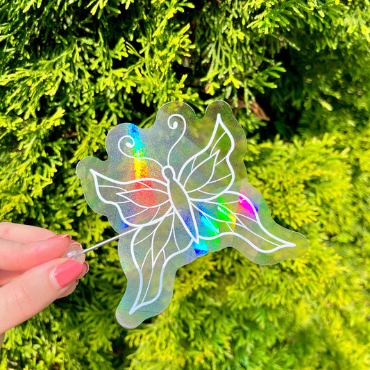 Holographic butterfly suncatcher sticker held in front of green foliage