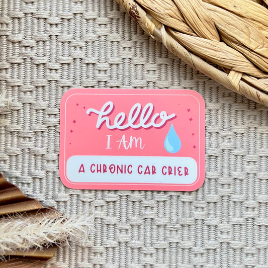 Pink sticker with text 'hello I am a chronic car crier' on a textured surface