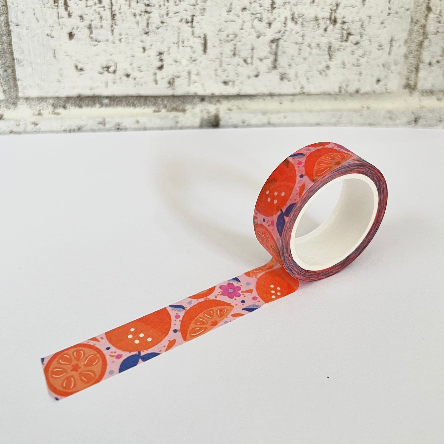 Decorative tape with an orange and floral pattern on a white surface with a brick wall background.