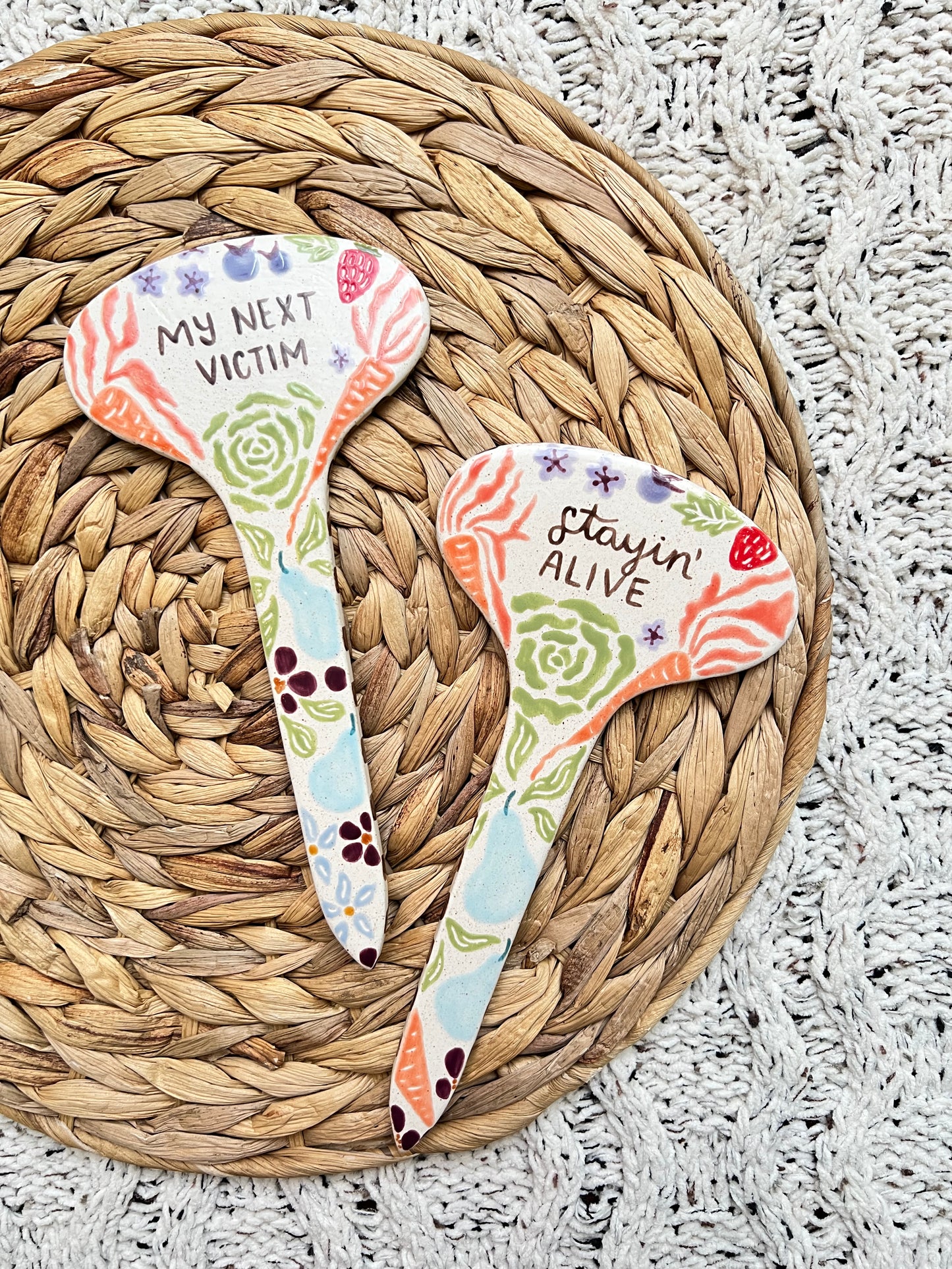 Two decorative ceramic garden stakes with floral designs and text on a woven mat.