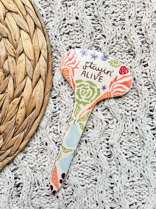 Colorful ceramic garden stake with 'Stayin' Alive' text on a textured surface