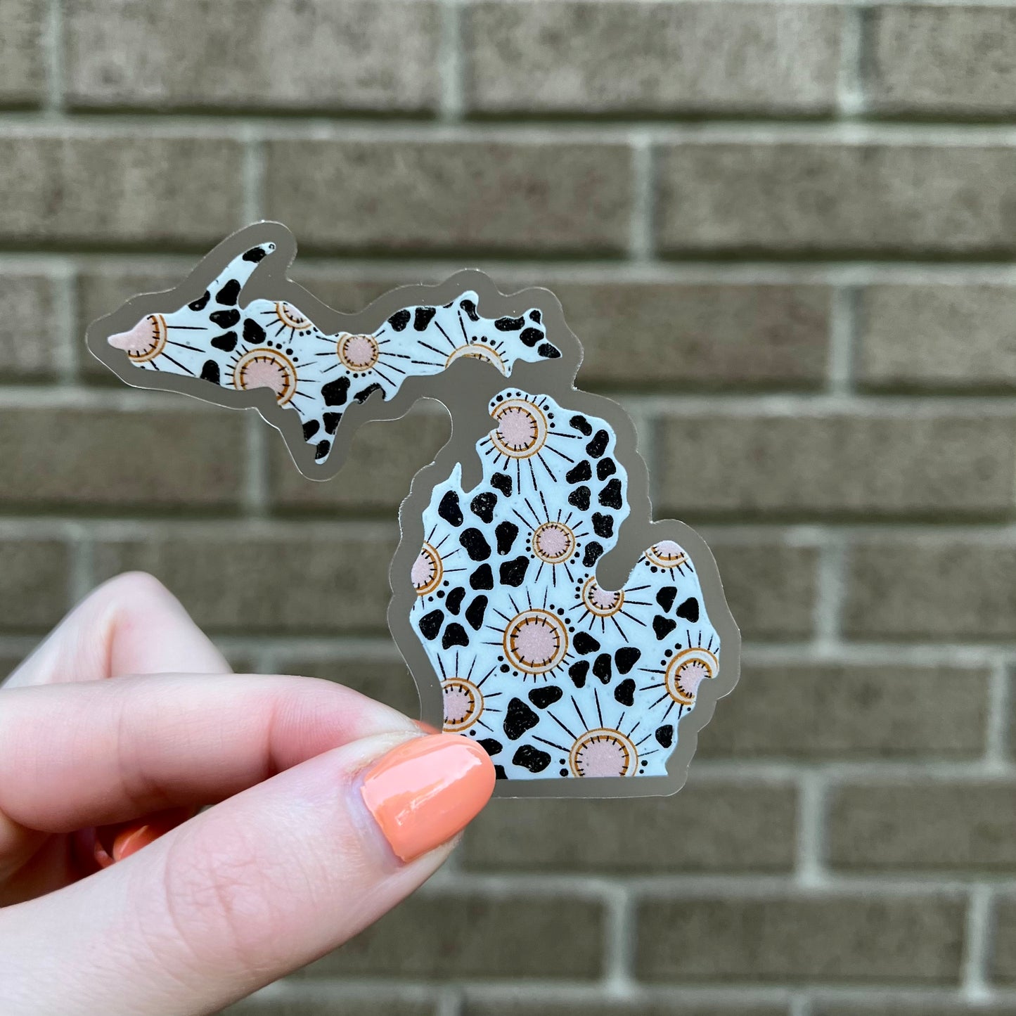 Decorative sticker shaped like the state of Michigan held by a hand against a brick wall.