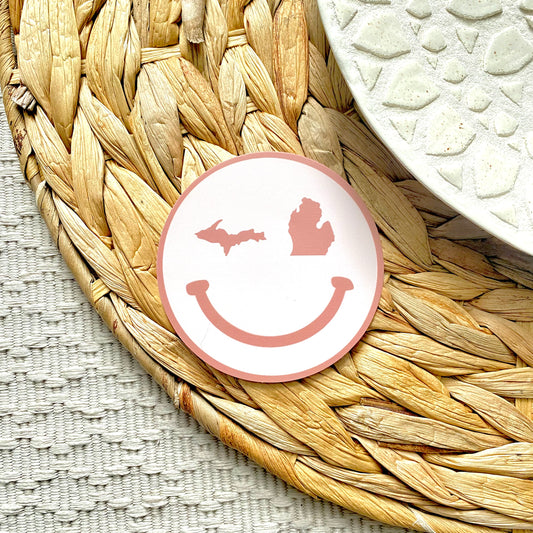 Round pink smiley face sticker on a woven mat