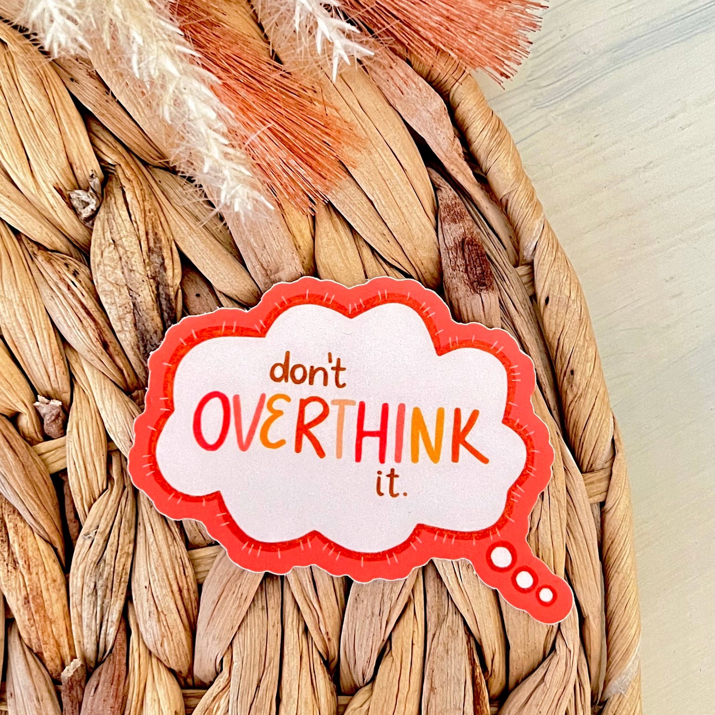 Speech bubble shaped sticker with 'don't overthink it' text on a woven background