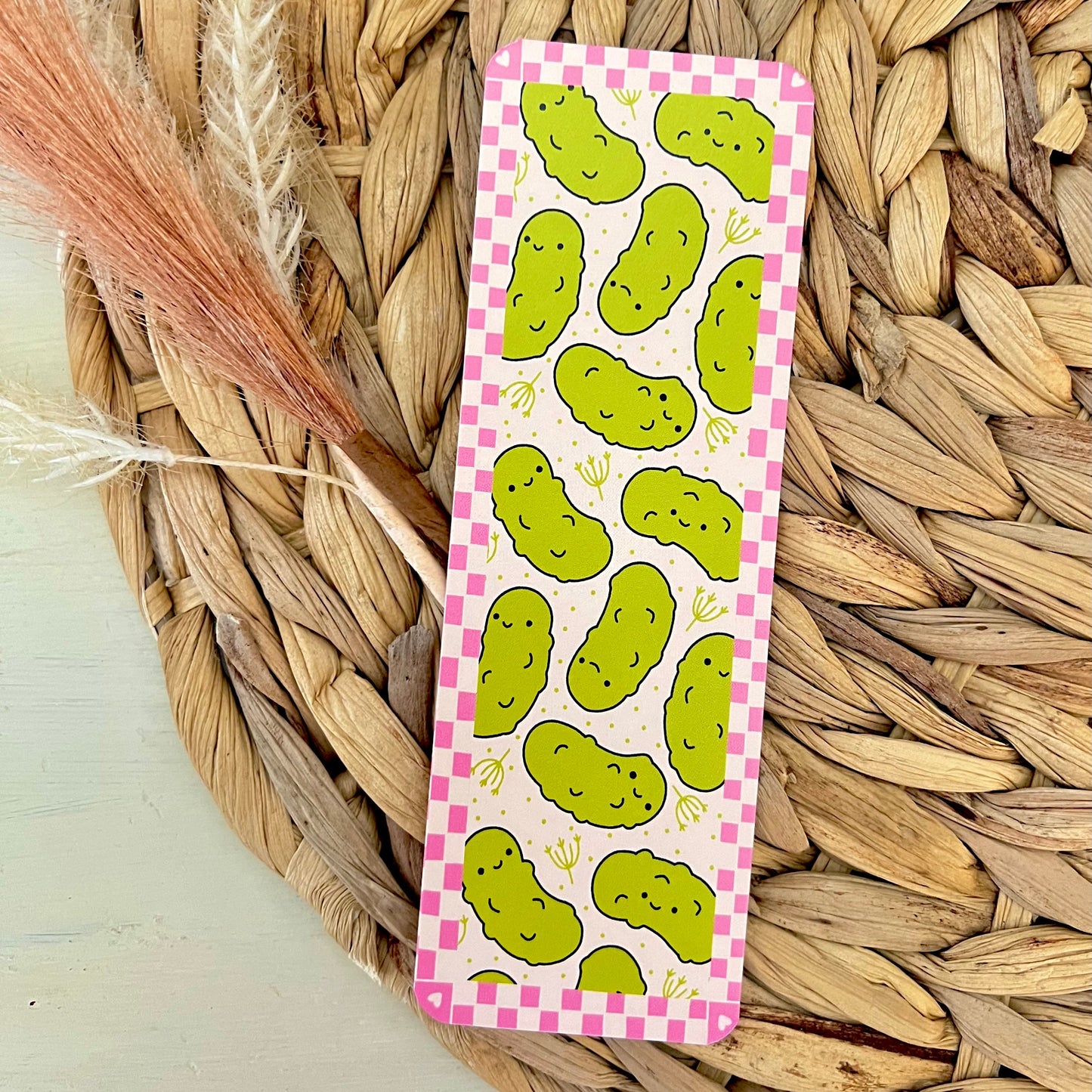 Bookmark with green pickle pattern on a pink checkered background, placed on a woven mat.