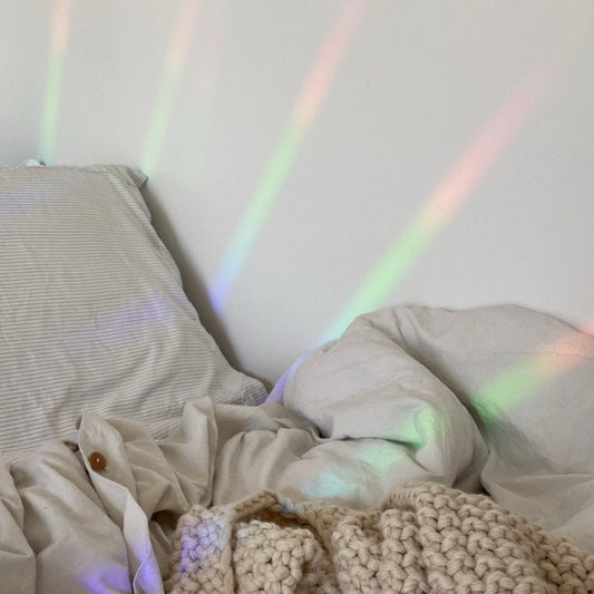 Neatly made bed with striped pillow and textured blanket, illuminated by soft rainbow lights.