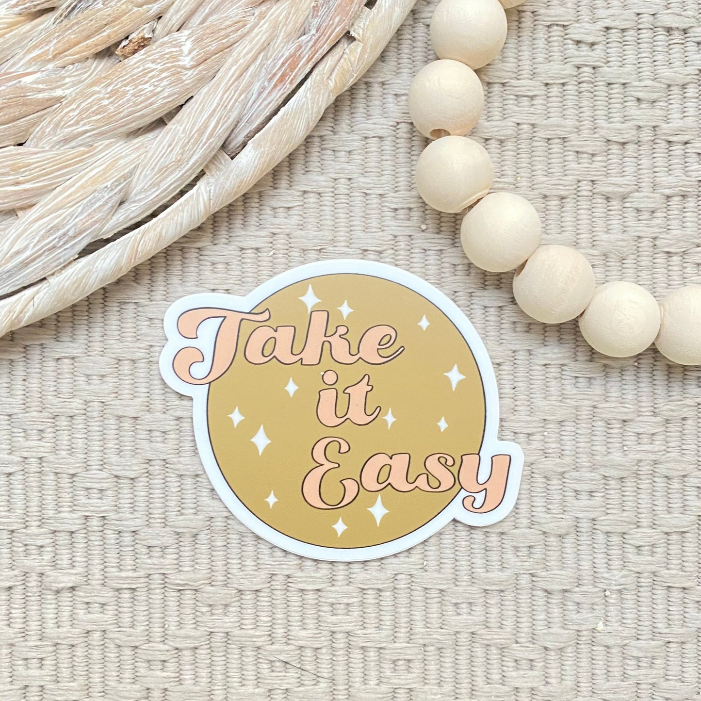 Sticker with 'Take it Easy' text on a textured surface with beads