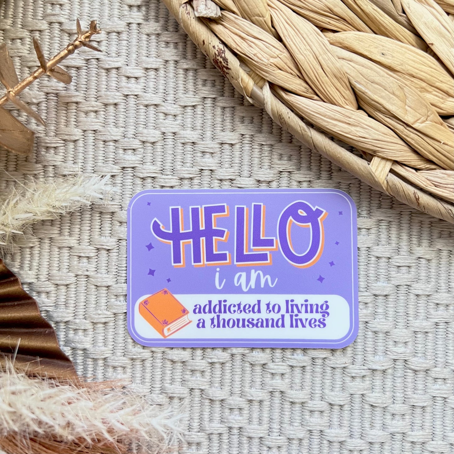 Purple sticker with text 'HELLO i am addicted to living a thousand lives' on a textured surface