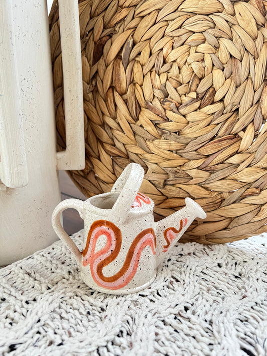 Small ceramic watering can planter with decorative design on a textured surface