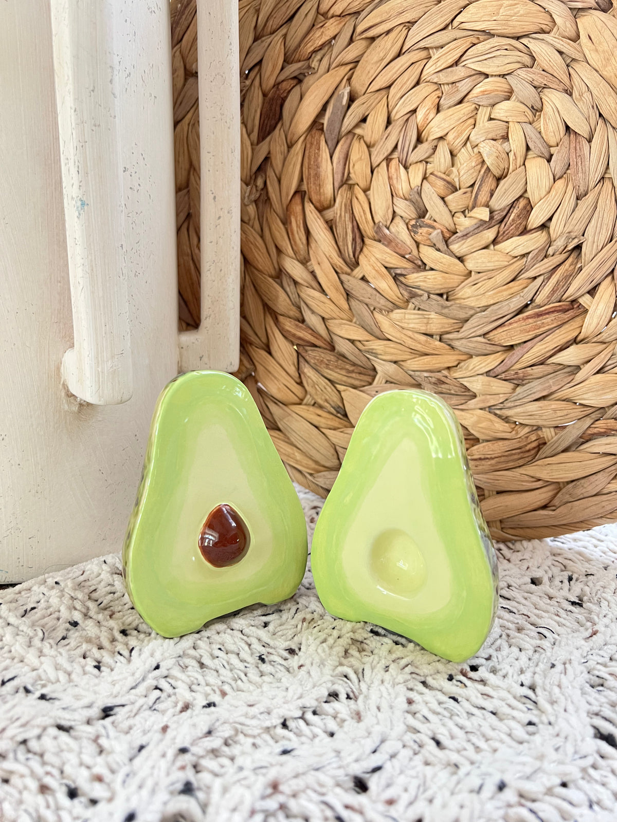Two green avocado-shaped objects on a textured surface with a woven mat in the background.