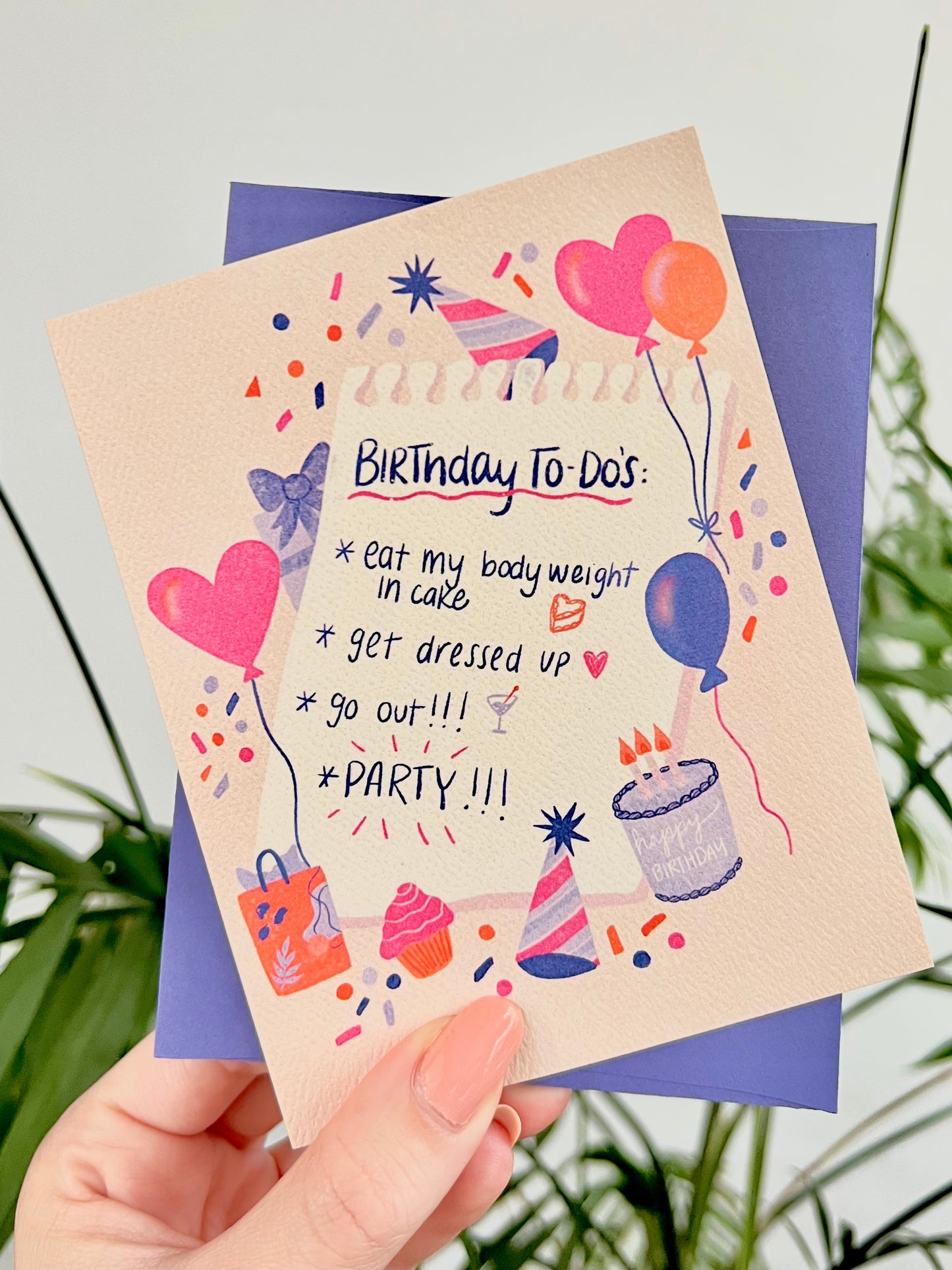 Birthday card with colorful illustrations and text held by a hand against a natural background