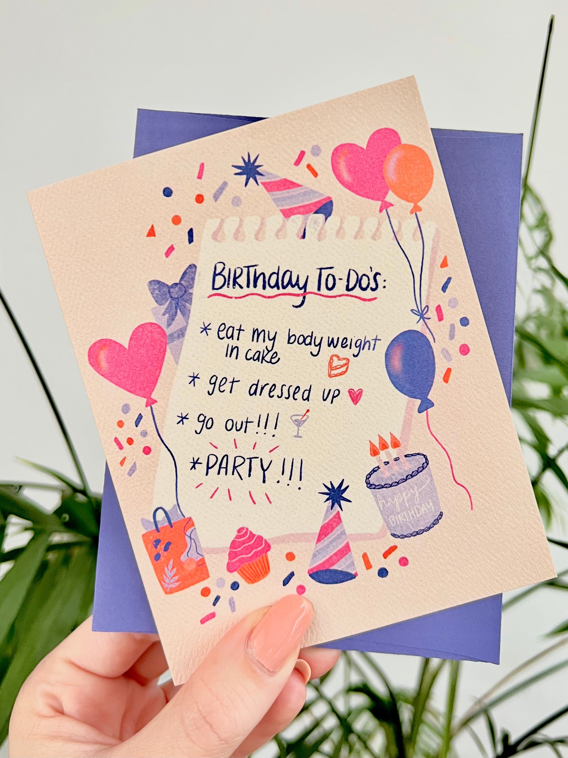 Birthday card with colorful illustrations and text held by a hand against a natural background