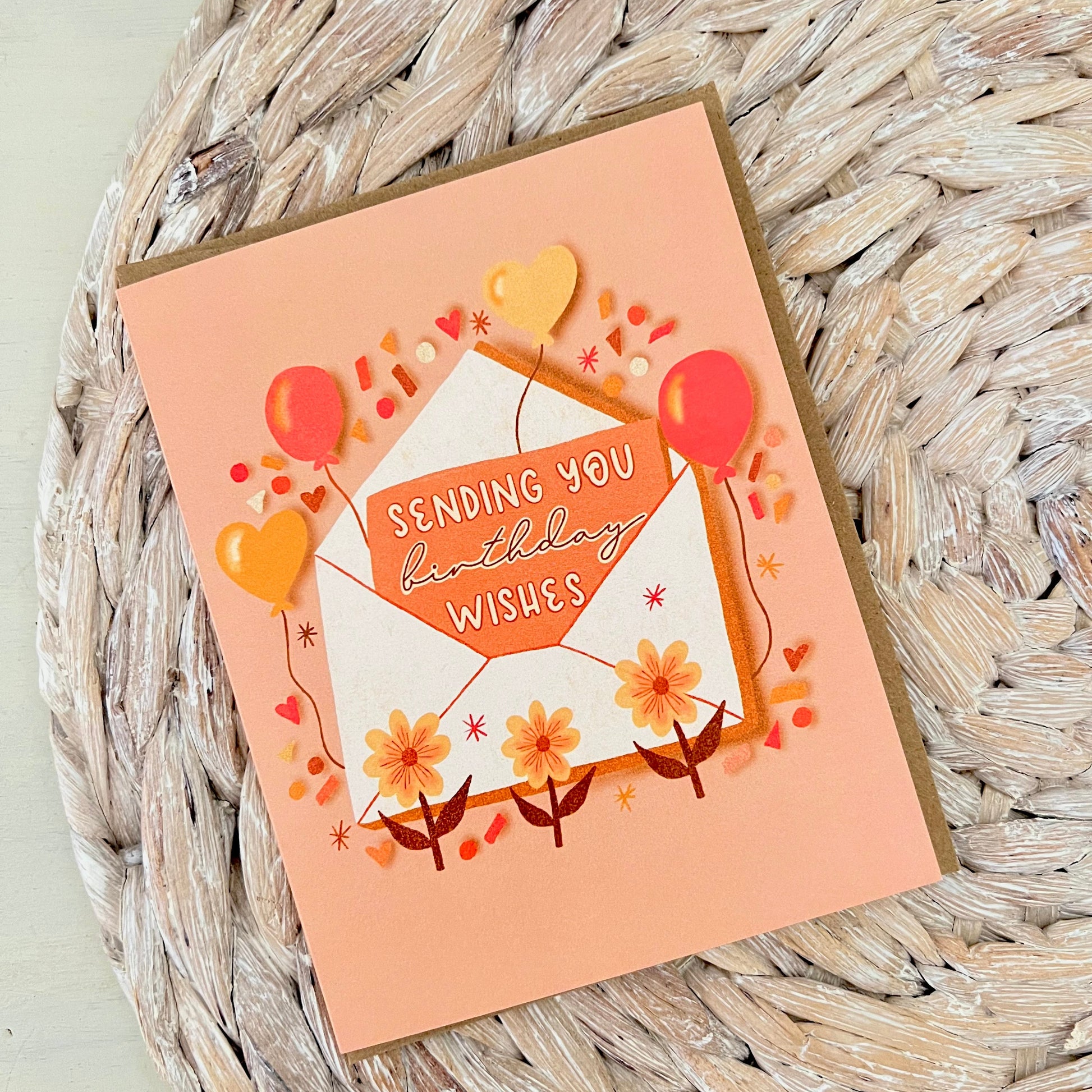 Greeting card with 'Sending you birthday wishes' text and an envelope and balloon illustration on a woven surface