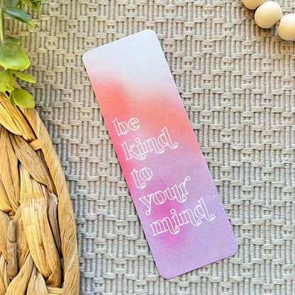 Gradient bookmark with 'be kind to your mind' text on a textured surface with plants and beads.