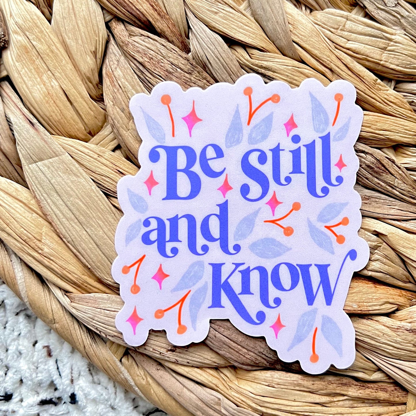 Sticker with 'Be still and know' text on a woven mat background