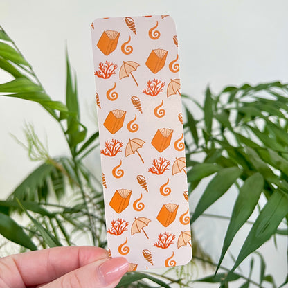 Beach themed bookmark held by a hand with a green leafy background