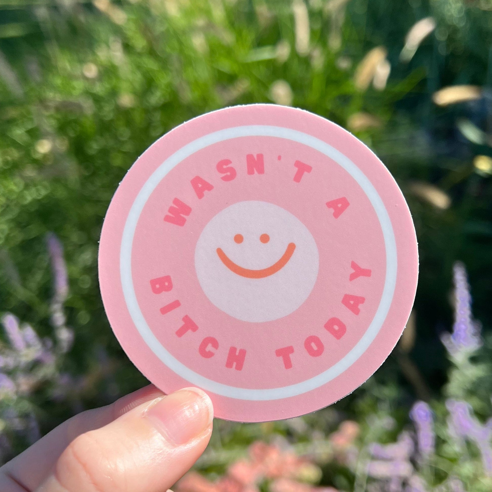 Pink sticker with text held by a hand against a blurred natural background