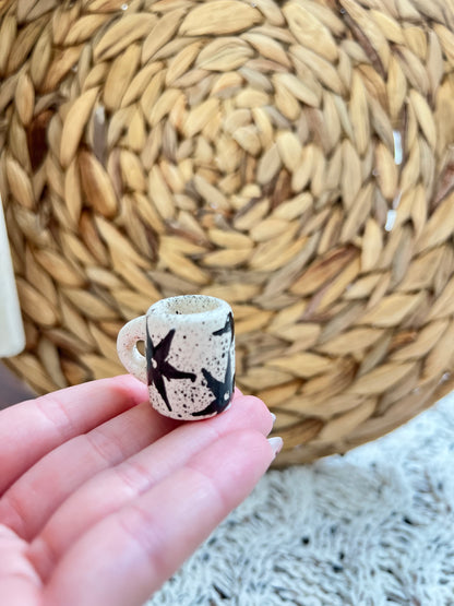 Small ceramic cup with black patterns held in a hand against a woven mat background