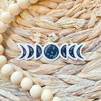 Set of black floral moon phase stickers on a woven surface with wood beads