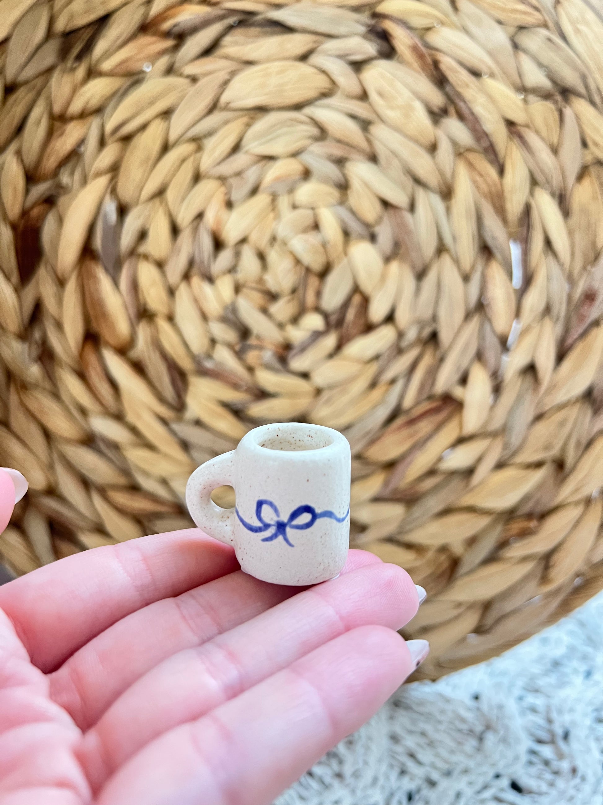 Small ceramic cup with a blue bow held in a hand against a woven mat background