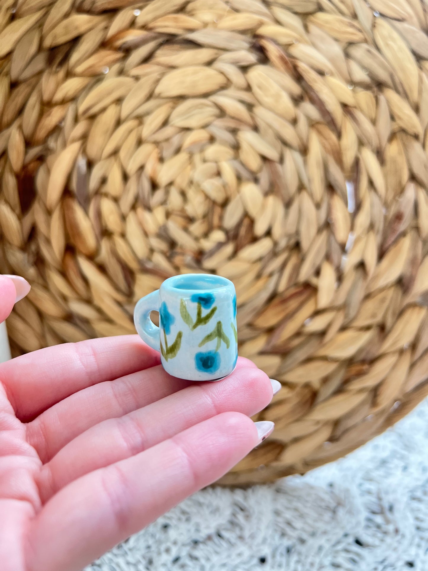 Small ceramic mug with floral design held in a hand against a woven mat background