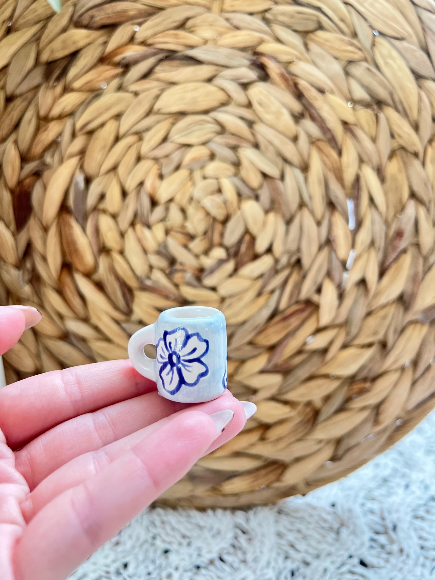 Small ceramic mug with a floral design held in front of a woven mat.