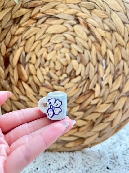 Small ceramic mug with a floral design held in front of a woven mat.