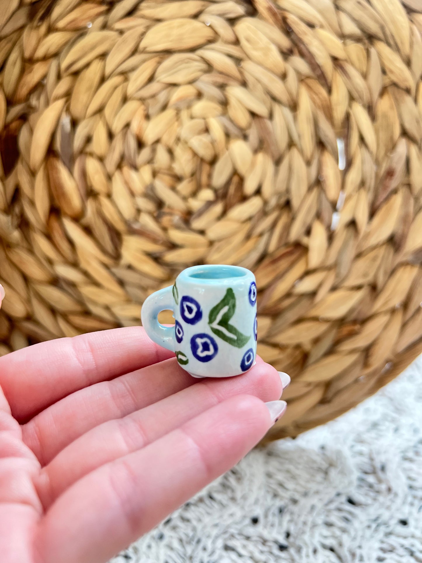 Small ceramic cup with blueberry design held in a hand against a woven mat background