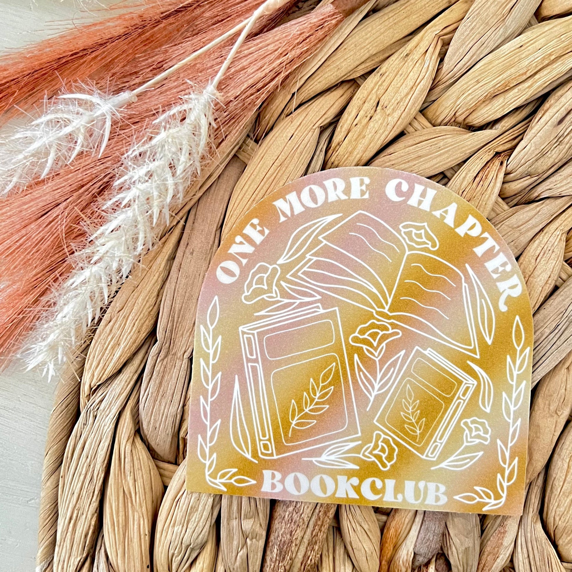 Sticker with 'One More Chapter' and 'BookClub' text on a woven background