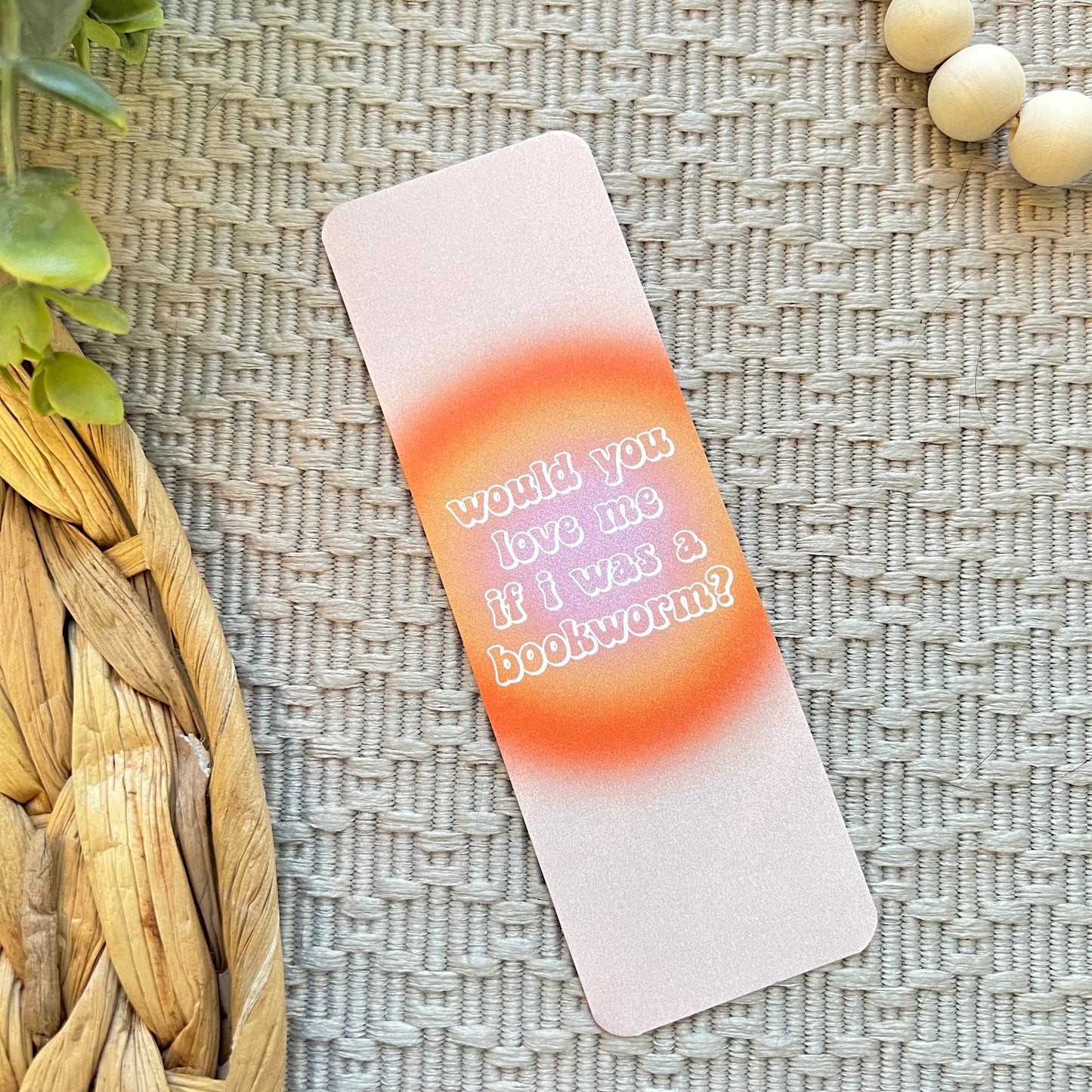 Gradient bookmark with "would you love me if I was a bookworm?" text on a textured surface with plants and beads