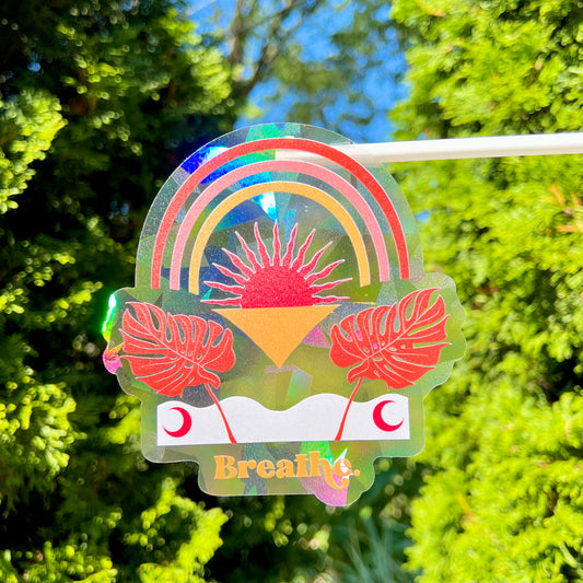 Holographic sticker with rainbow, sun, and leaves design on a green leafy background