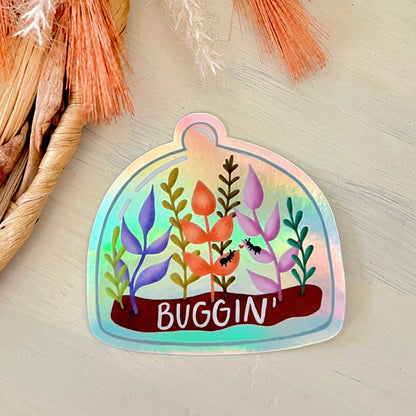 Holographic sticker of terrarium with colorful plants and 'Buggin' text on a textured surface