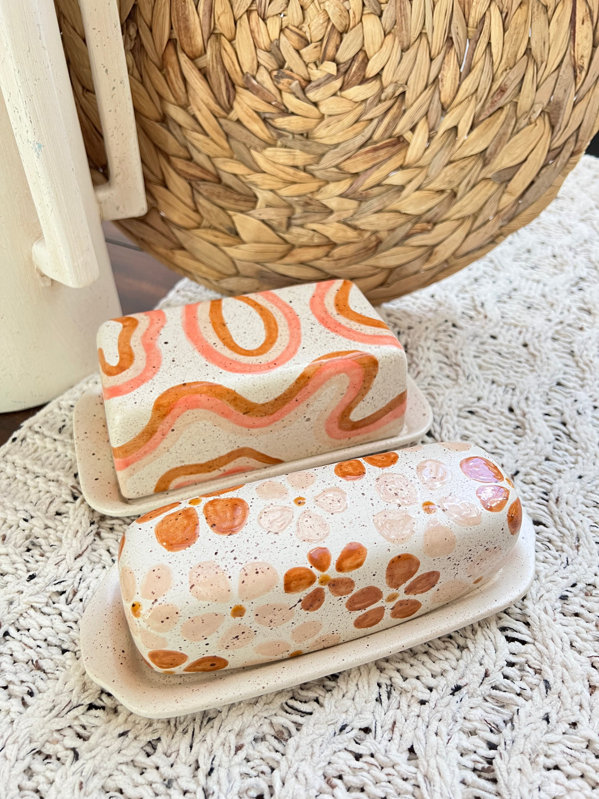 Two ceramic butter dishes with decorative patterns on a textured surface.