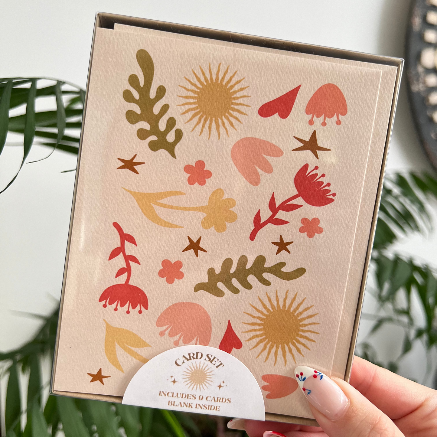 Card with floral and abstract designs held by a hand against a plant background