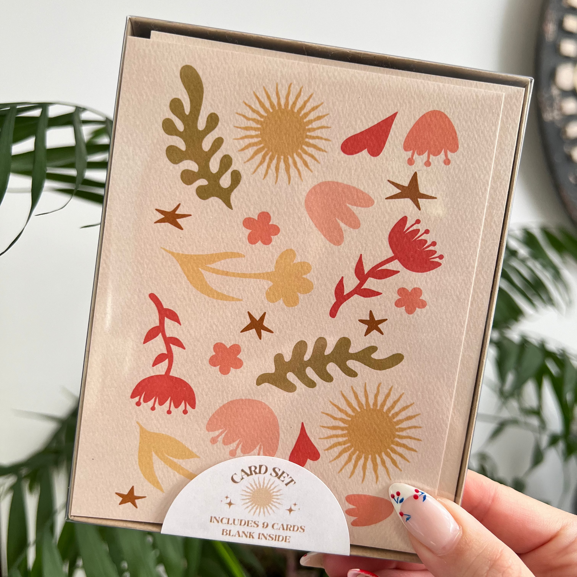 Card with floral and abstract designs held by a hand against a plant background