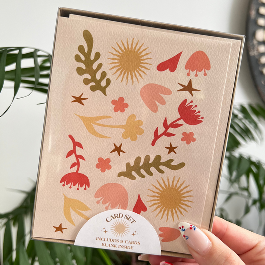 Card with floral and abstract designs held by a hand against a plant background