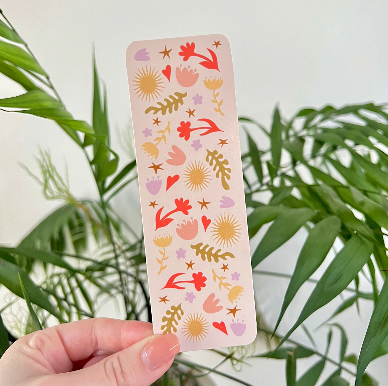 Bookmark with colorful abstract pattern on it held by a hand with a plant in the background