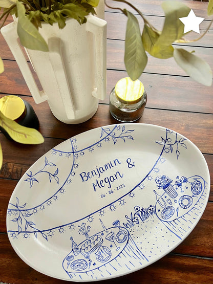Decorative plate with blue designs and text on a wooden surface with a pitcher and candle in the background.