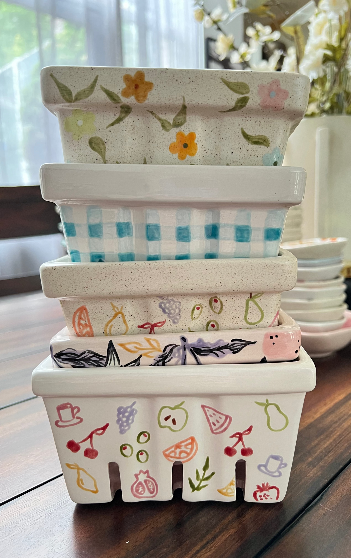 Stack of decorative ceramic berry baskets with floral and checkered patterns on a wooden surface.