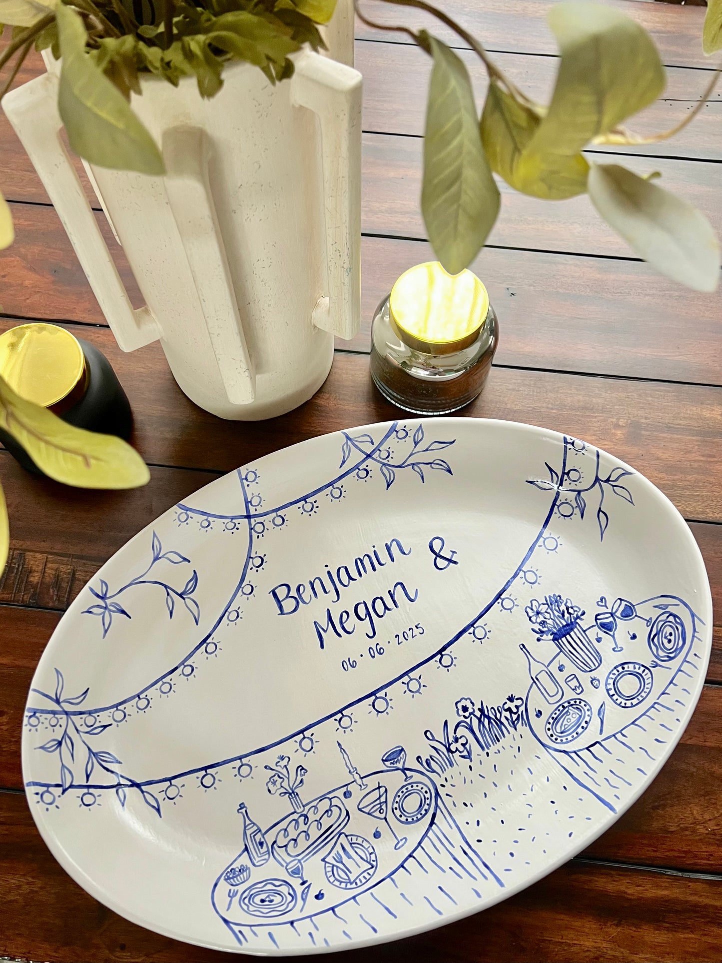 Decorative ceramic tray with blue designs and text sitting on a wooden surface with a plant and candle.