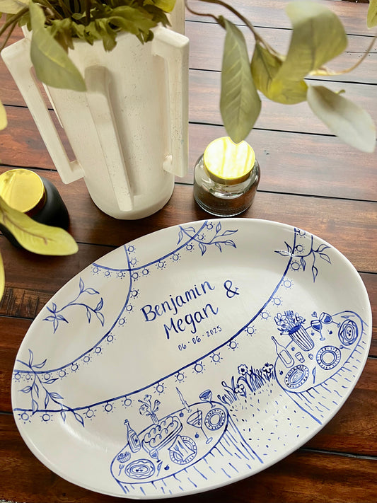 Decorative ceramic tray with blue designs and text sitting on a wooden surface with a plant and candle.