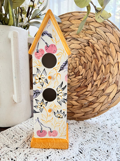 Decorative birdhouse with floral and cherry design on a textured surface.