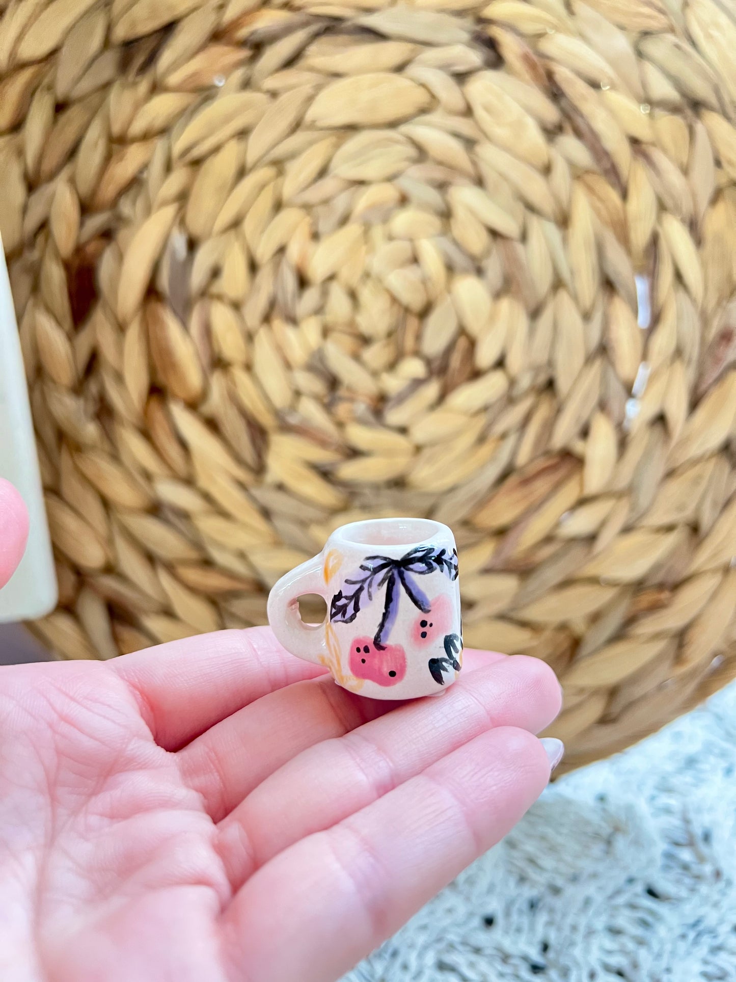Small decorative cup held in a hand against a woven mat background