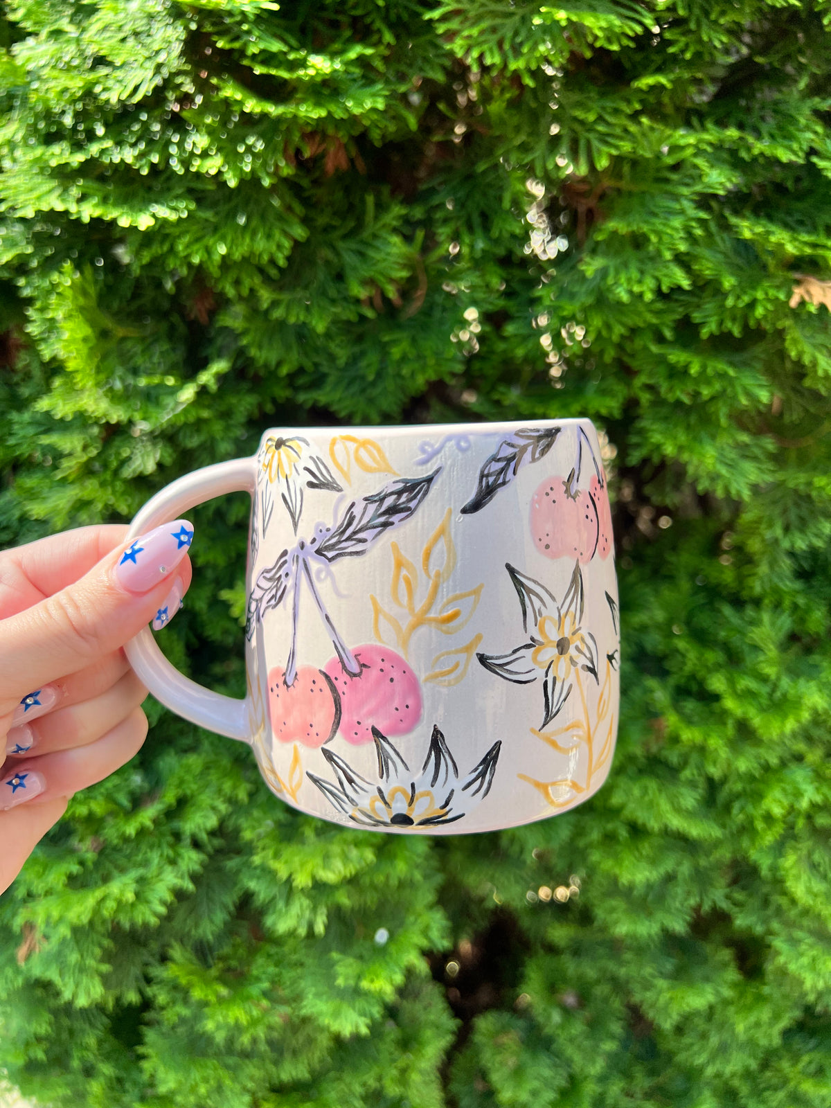 Hand holding a floral mug with a green bush background