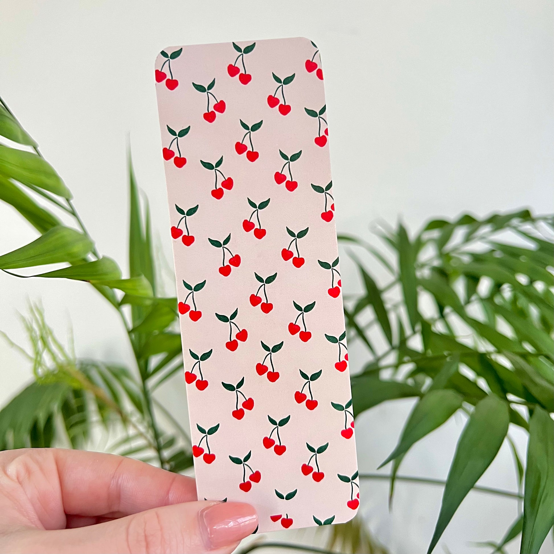 Bookmark with cherry pattern held by a hand in front of green plants