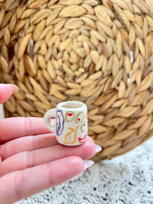 Small ceramic mug with colorful designs held by a hand against a woven basket background