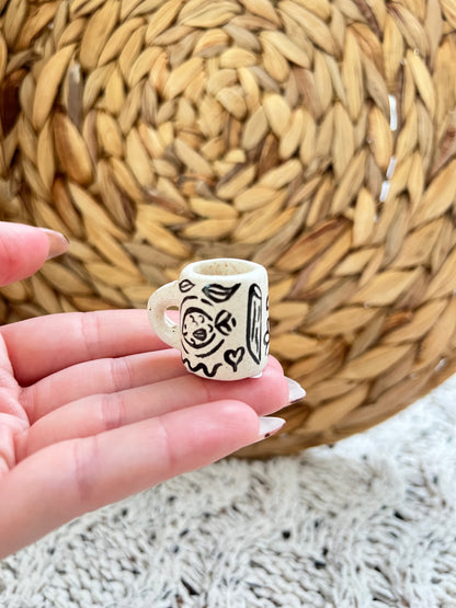 Small ceramic mug charm held between fingers with woven mat in background