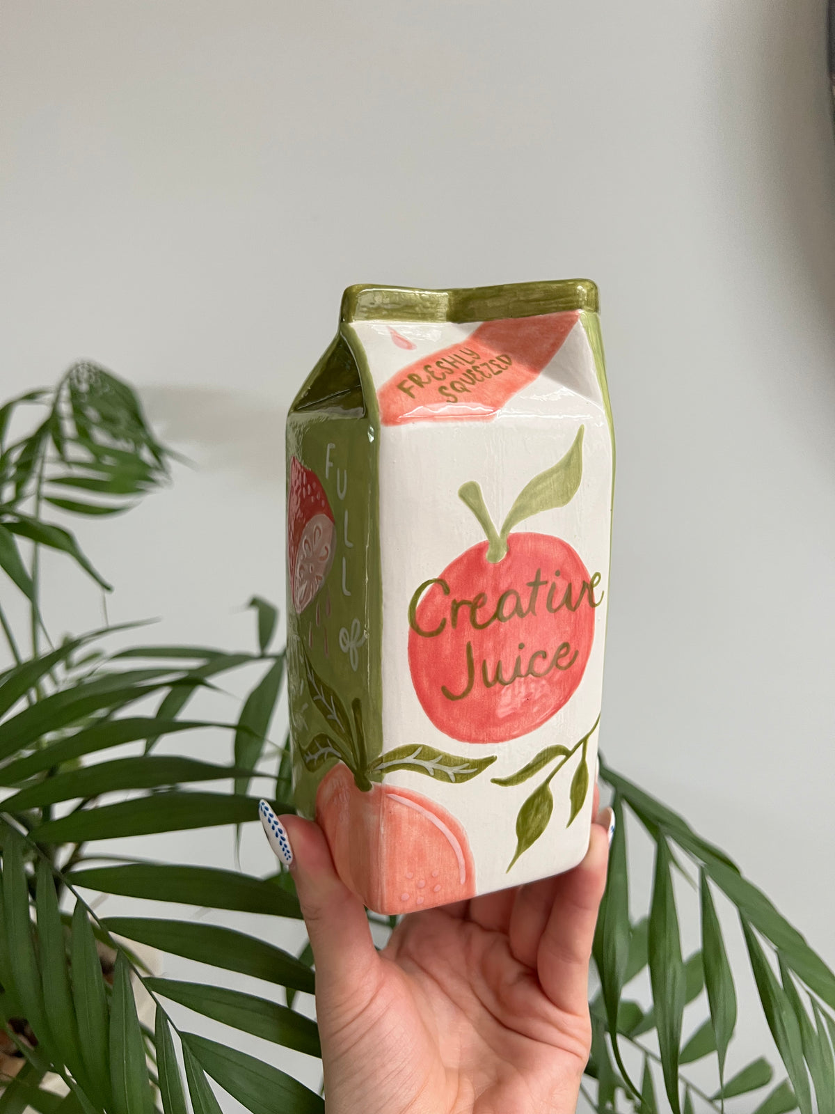 Hand holding a carton of 'Creative Juice' with a plant in the background