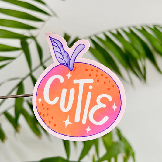 Sticker with 'Cutie' clementine design on a leafy background